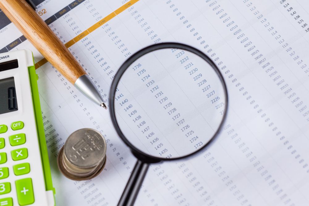 Lupe, Stift und Taschenrechner auf Dokument mit Zahlenreichen