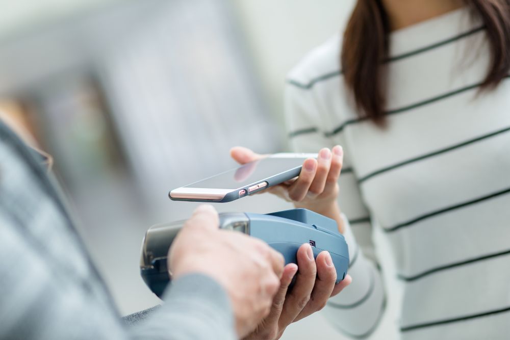 Bezahlterminal und Frau welche mit Handy digital zahlt