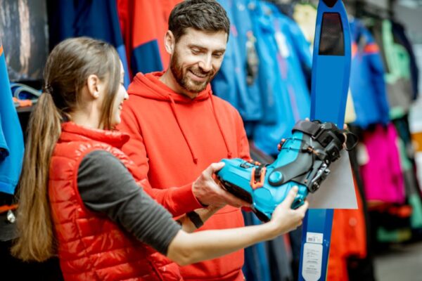 Verkäuferin zeigt Kunden unterschiedliche Modelle eines Skischuhes welche im Kassensystem für Sportwarenhändler registriert sind