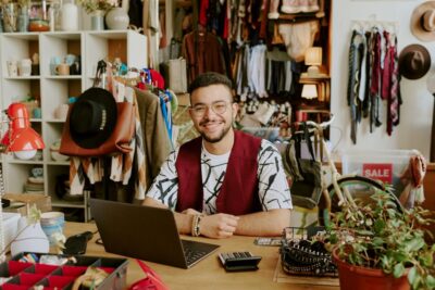 glücklicher Inhaber eines Second Hand Geschäftes der seinen Onlineshop auf dem Laptop verwaltet