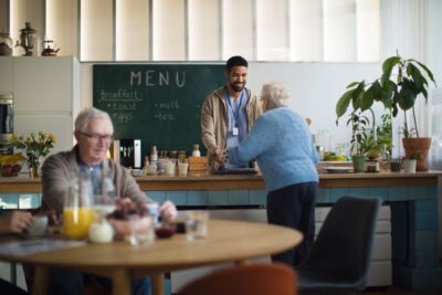 Seniorin holt essen bei der Essensausgabe und unterhält sich mit dem Mitarbeiter